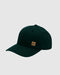 A dark forest green baseball cap with a small tan square patch on the front, photographed on a light gray background.